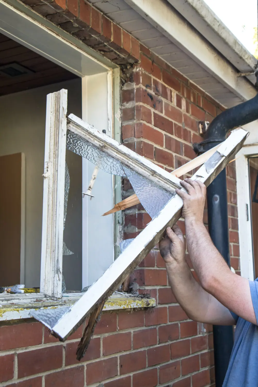 Arbeiter entfernt während der Hausrenovierung alten hölzernen Fensterrahmen von einer Ziegelwand