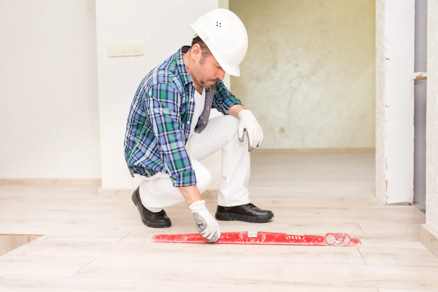 Ein Bauarbeiter mit Schutzhelm prüft bei Reparaturen beim Hausbau die Ebenheit der Fliesen auf dem Boden