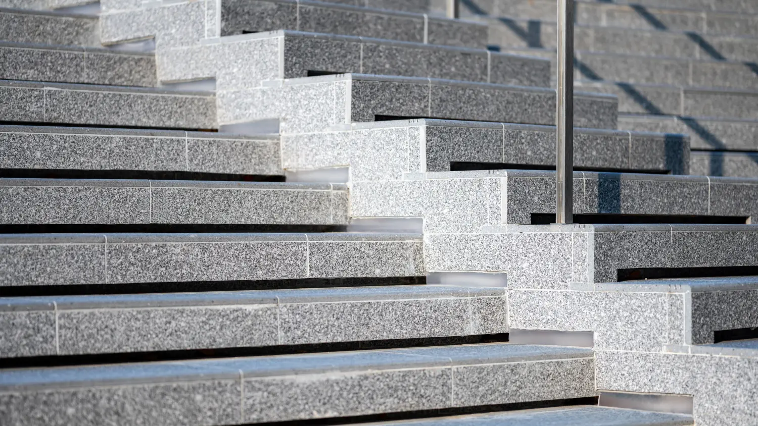 Betontreppe im Freien mit rauen Granitfliesen bedeckt. Stufe der Außentreppe mit Edelstahlgeländer.